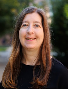 woman with long brown hair in black shirt with building blurred in background