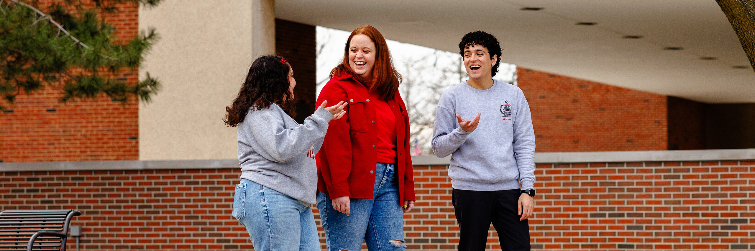 Three students smile while talking to each other on the quad.